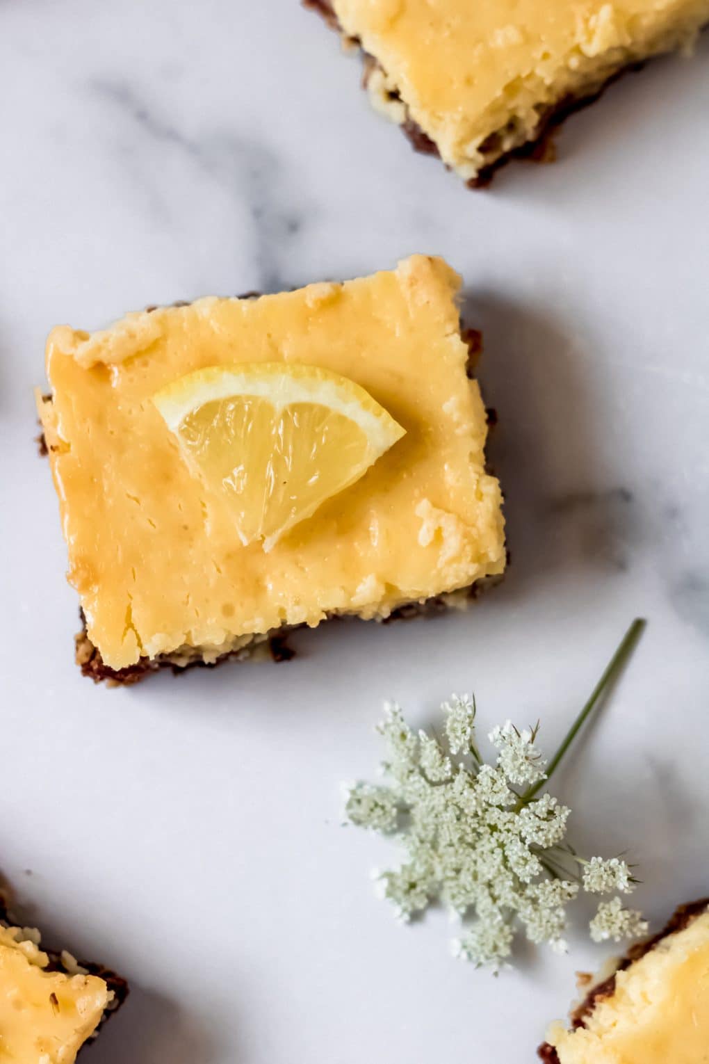 gluten-free lemon bars cut into squares on a table with a white flower nearby