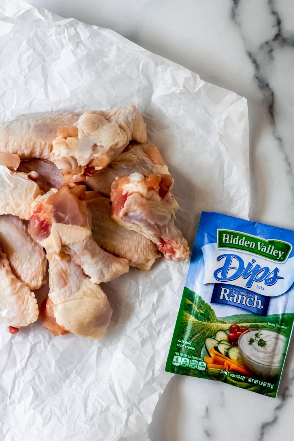 raw chicken wings on a piece of white parchment paper and a packet of ranch dressing
