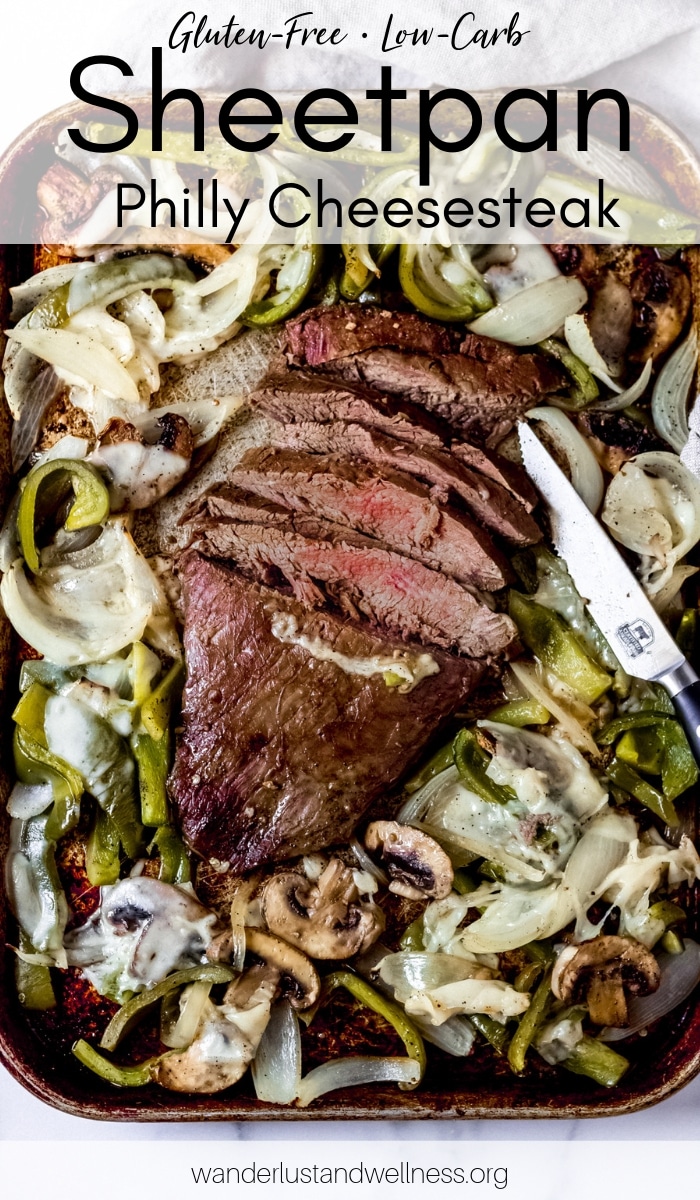 a flank steak in the center of a baking sheet with peppers, onions and mushrooms surrounding it for a sheet pan Philly cheesesteak