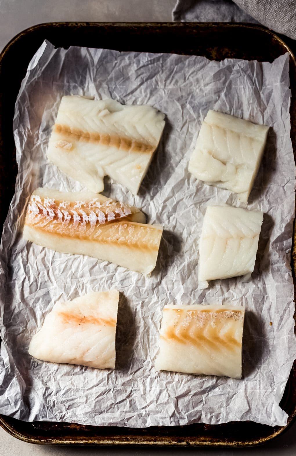 6 raw cod fillets on a sheet of parchment paper on a sheet pan
