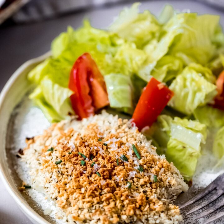 a parmesan crusted cod fillet on a white plate with a side salad