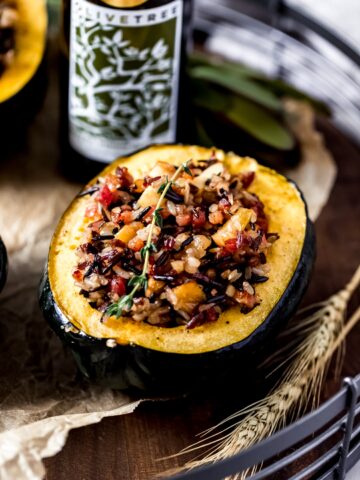 a stuffed acorn squash on a wooden serving tray with a bottle of rosemary olive oil in the background