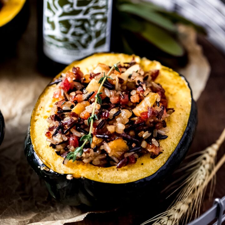 a stuffed acorn squash on a wooden serving tray with a bottle of rosemary olive oil in the background