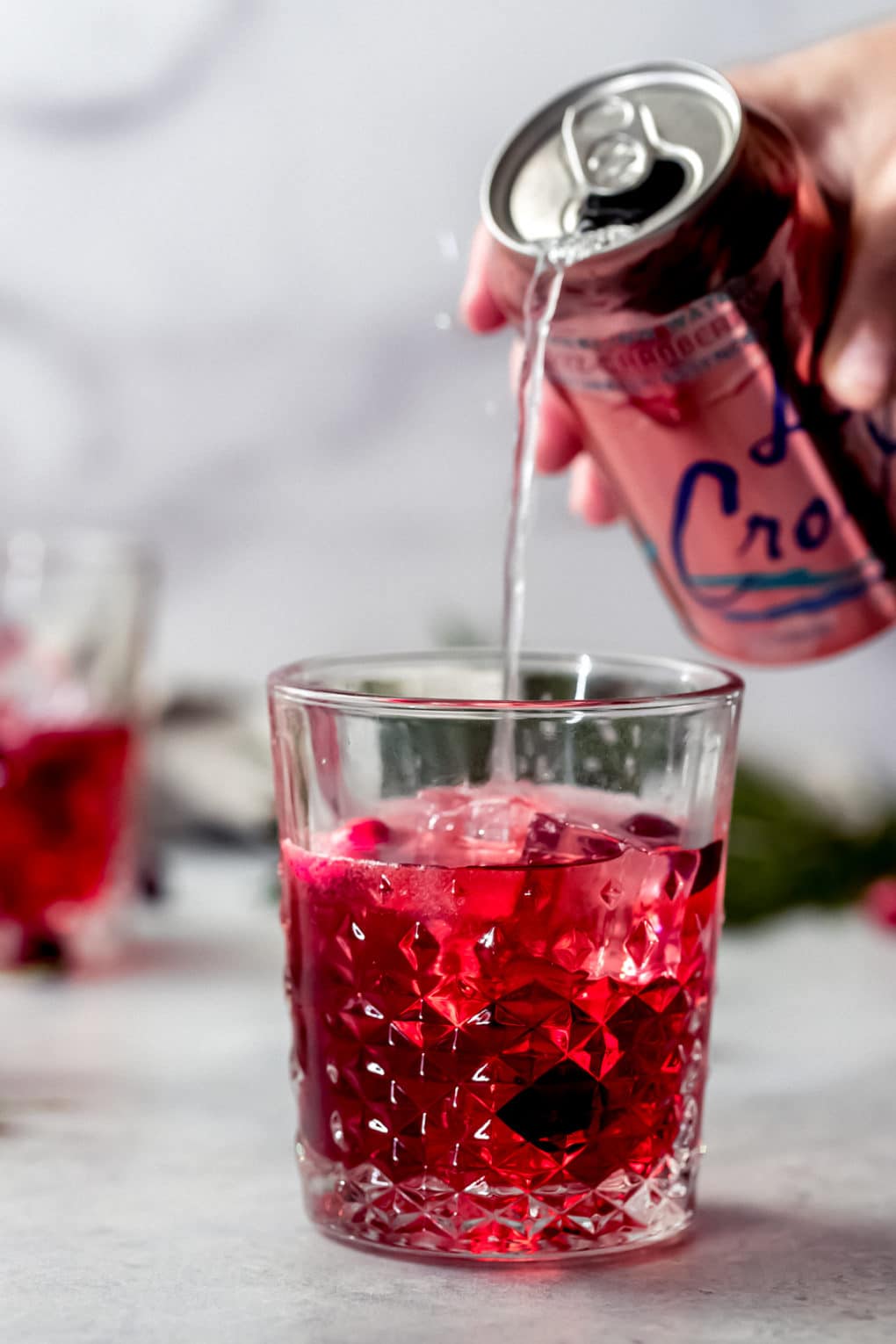 a woman pouring La Croix bran-raspberry into a La Croix vodka cranberry 