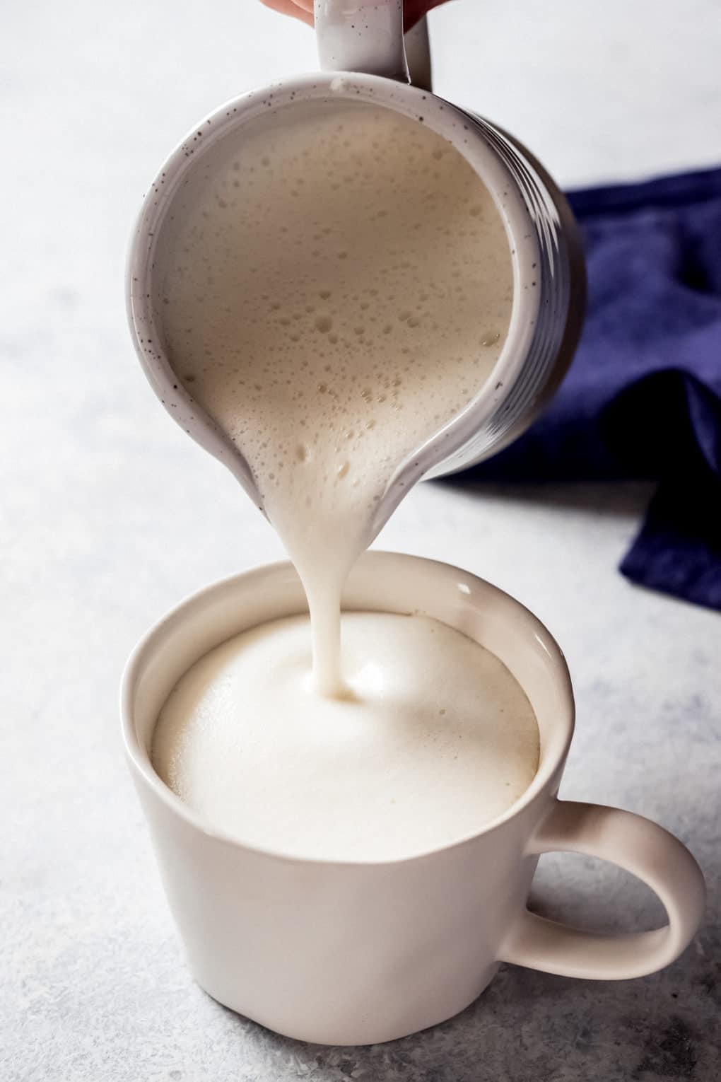 a person pouring frothed heavy cream over earl grey tea for a London Fog latte