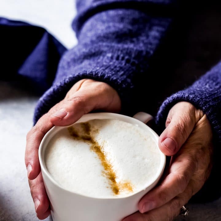a woman wearing a blue sweater with her hands around a mug of London Fog