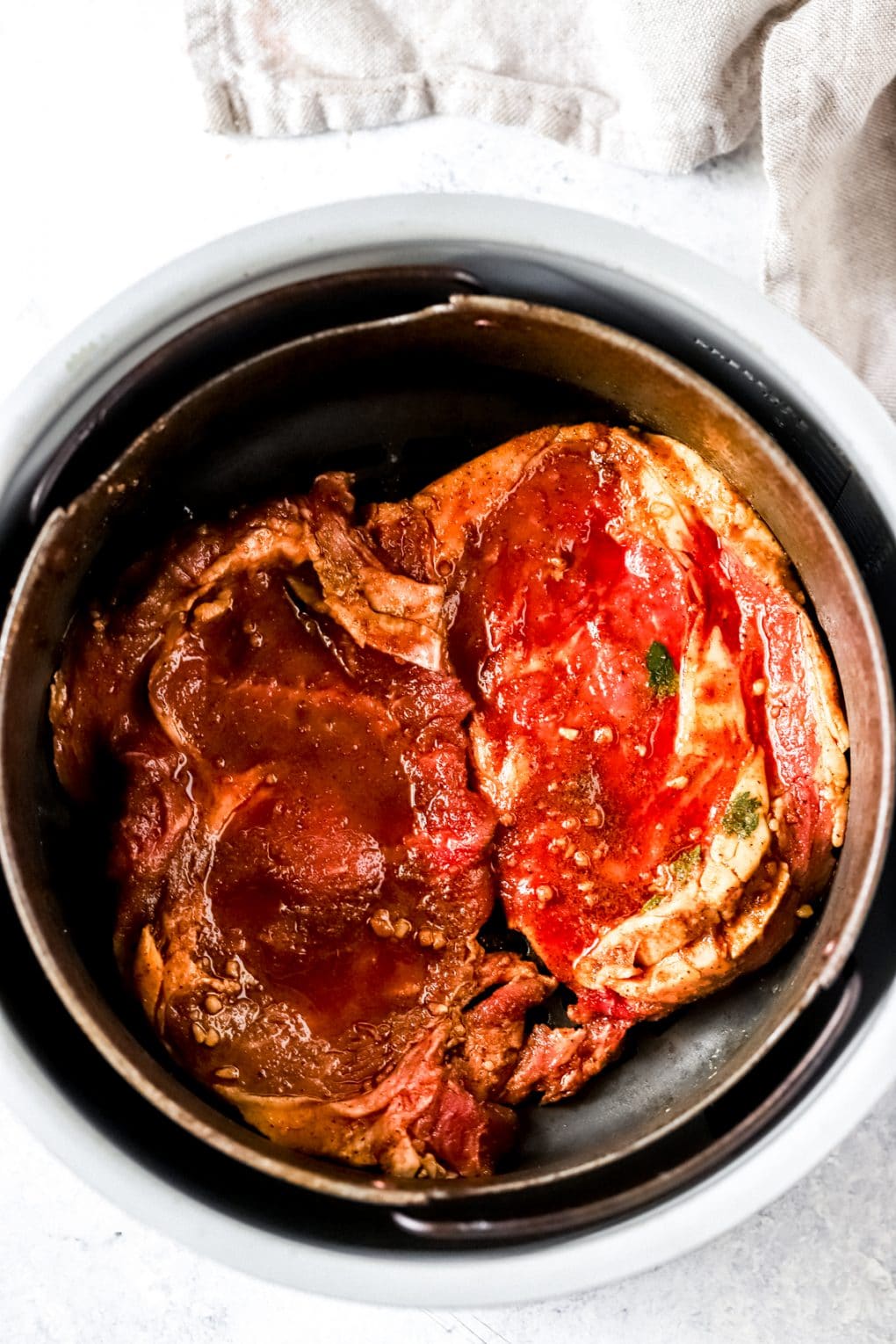 marinated thin-cut ribeye steaks in an air fryer basket ready to cook