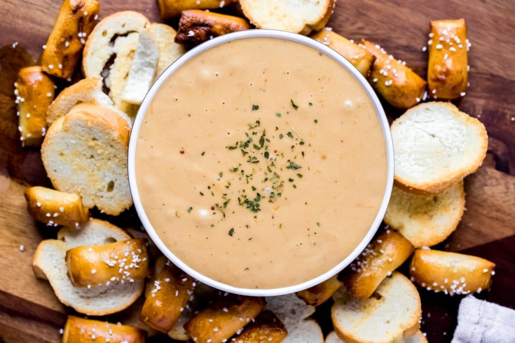 a bowl of Guinness beer cheese dip surrounded by pretzels and crostini