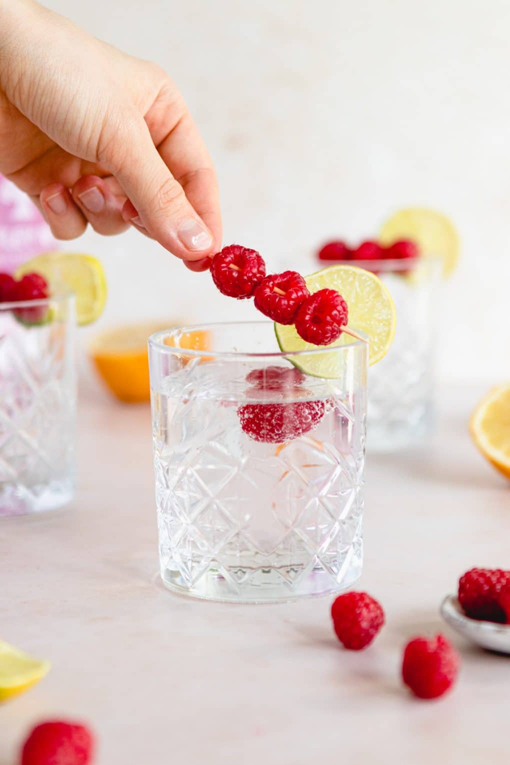 a woman adding fresh berries to a berry la Croix cocktail