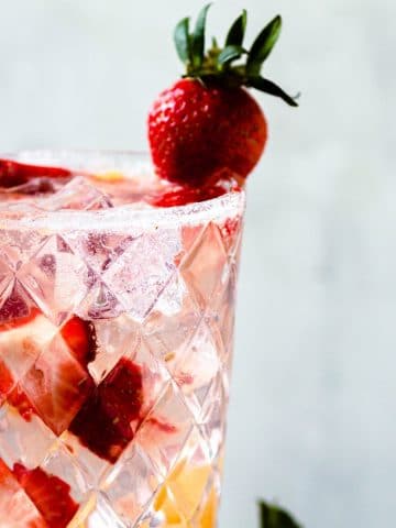 a tall glass of a pineapple strawberry cocktail with fresh strawberries