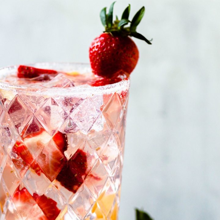 a tall glass of a pineapple strawberry cocktail with fresh strawberries