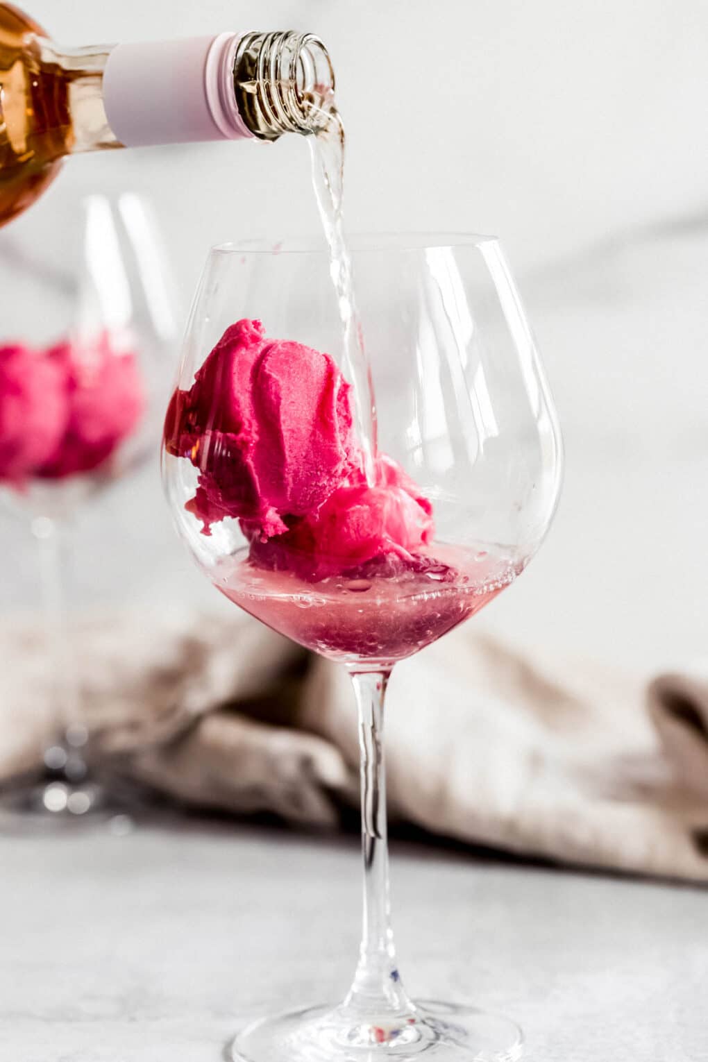 a person pouring rosé wine into a wine glass with raspberry sorbet