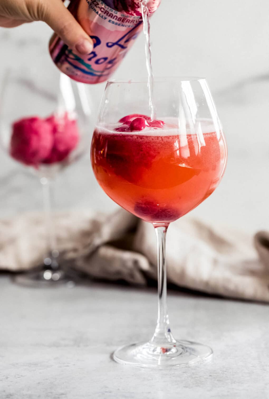 a person pouring cran-raspberry la croix into a wine glass