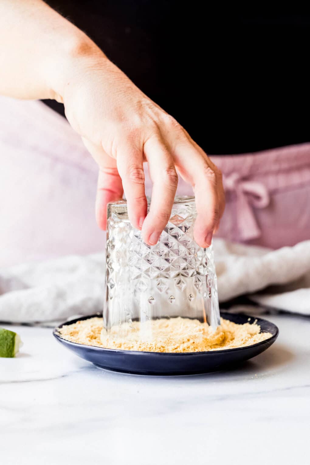 A woman dipping glass rim into graham cracker crumbs